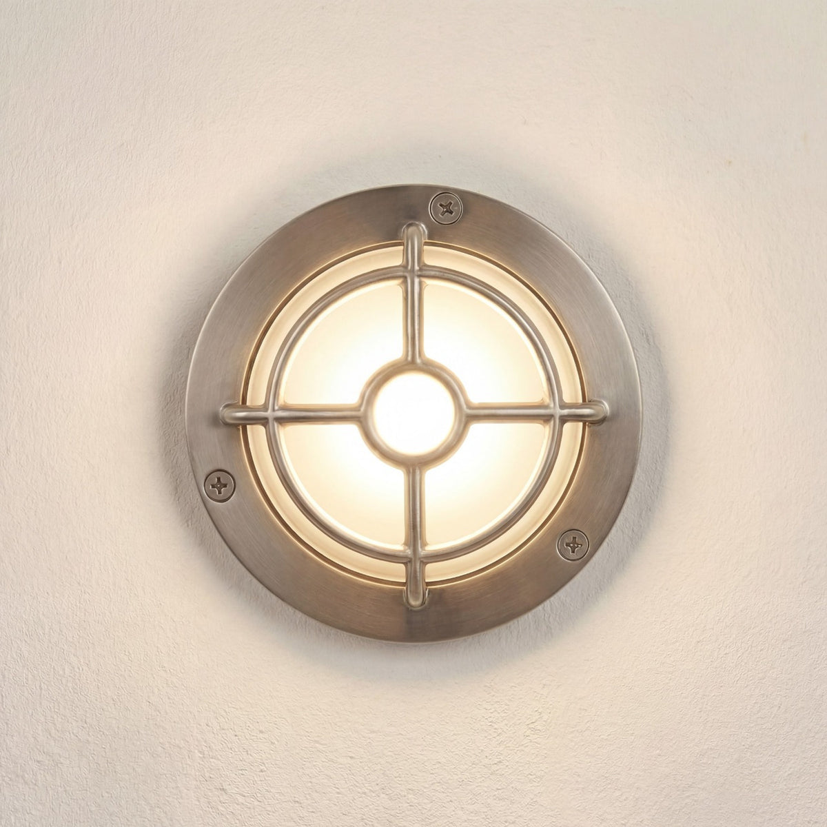 Walkway Guard IP65 outdoor wall light in satin nickel, round brass body with cross-and-ring guard over a glowing frosted glass diffuser, shown on a plain light wall.