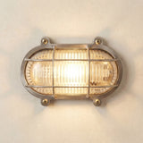 Merchant Flush Oval Bulkhead Light in satin nickel, showing the ribbed glass diffuser under a barred cage with visible mounting screws, lit against a plain wall.