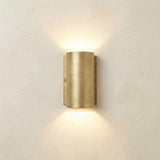 Pharos Compact Outdoor Up & Down Wall Light in raw brass, a half-cylinder fixture on a slim wall plate with visible screws, casting light up and down on a plain light background.