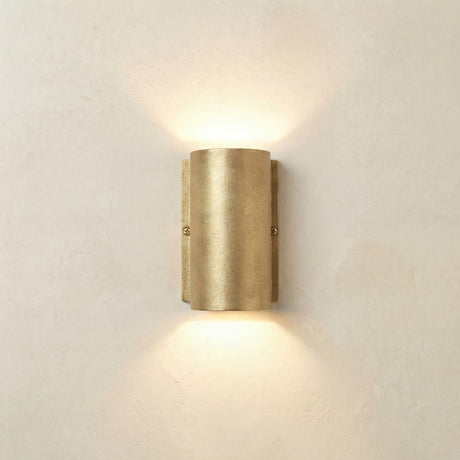 Pharos Compact Outdoor Up & Down Wall Light in raw brass, a half-cylinder fixture on a slim wall plate with visible screws, casting light up and down on a plain light background.