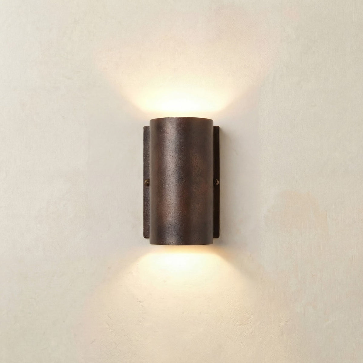Pharos Compact Outdoor Up & Down Wall Light IP44 in antique brass, a rounded cylindrical fixture on a slim wall plate casting light upward and downward, shown against a plain light wall.