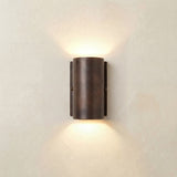 Pharos Compact Outdoor Up & Down Wall Light IP44 in antique brass, a rounded cylindrical fixture on a slim wall plate casting light upward and downward, shown against a plain light wall.