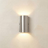 Pharos compact outdoor up & down wall light in satin nickel, a solid brass cylinder on a flat back plate casting warm light upward and downward on a plain wall.