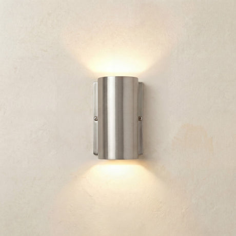 Pharos compact outdoor up & down wall light in satin nickel, a solid brass cylinder on a flat back plate casting warm light upward and downward on a plain wall.
