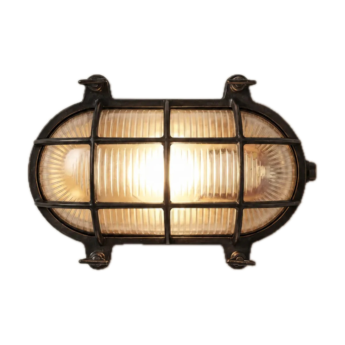 Horatio oval bulkhead light in blackened brass, with ribbed glass behind a grid-barred brass cage and corner fixing lugs, lit, on a plain white background.