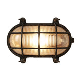 Horatio oval bulkhead light in blackened brass, with ribbed glass behind a grid-barred brass cage and corner fixing lugs, lit, on a plain white background.