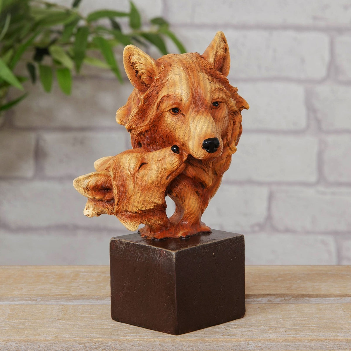 Adult and Cub Wolves Bust wood effect resin figurine in honey-brown with grained fur detail, glossy eyes and nose, set on a square dark plinth against a brick wall.