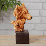 Adult and Cub Wolves Bust resin figurine in honey-brown wood-effect finish with fine grain detail, amber eyes and black noses, set on a dark block base against a brick wall.