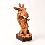 Two Giraffes Hand Painted Wood Effect Resin Figurine in brown, showing an adult giraffe curved over a seated calf on a dark rectangular base, set against a plain white background.