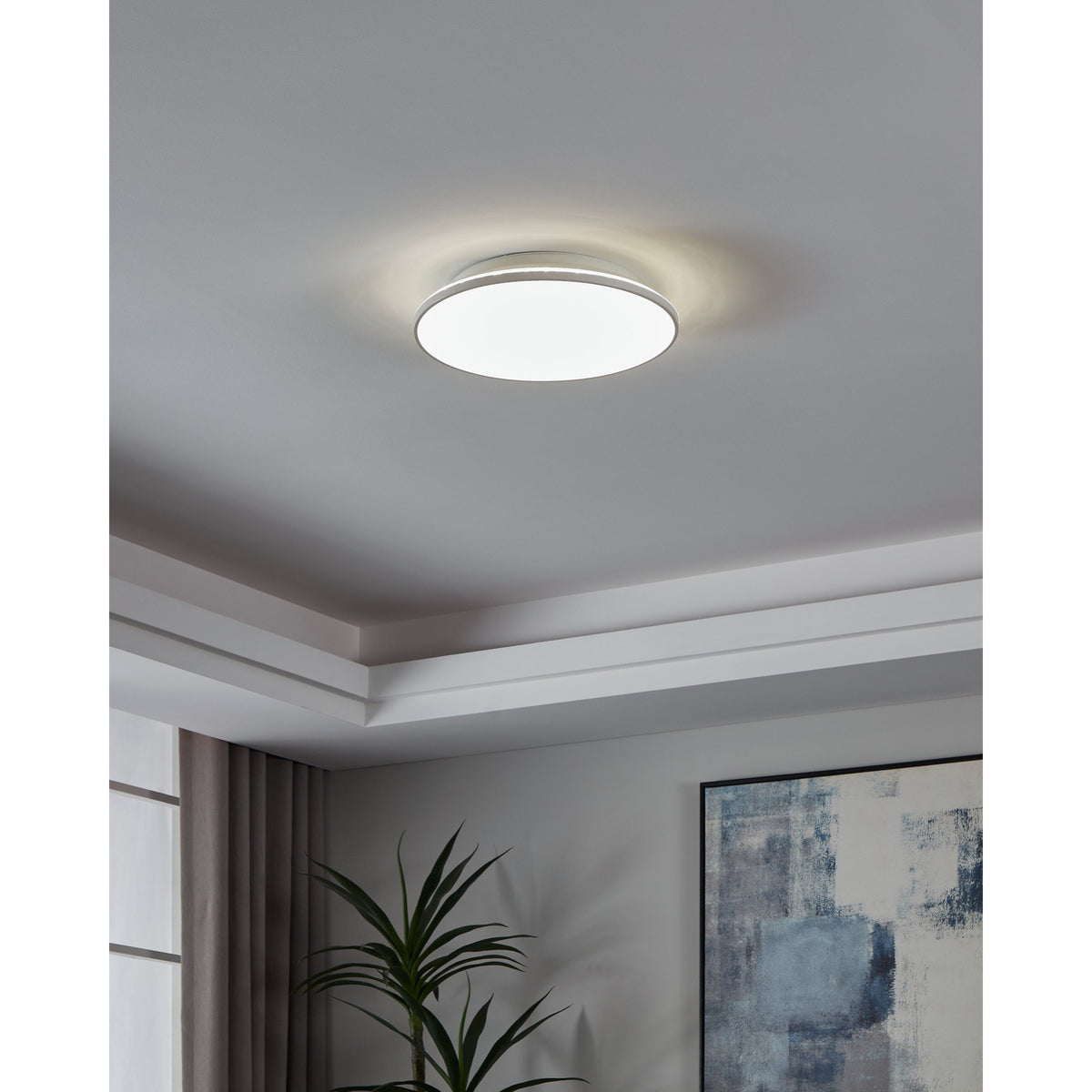 Nelbenne LED Downlight 38cm in white, round and slim with an opal diffuser, mounted on a grey ceiling in a room with cove lighting, a plant, and framed art visible below.