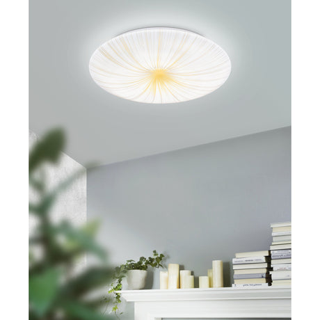 Nieves 1 LED flush ceiling light, 31cm round white fixture with domed diffuser and gold starburst lines, shown on a grey ceiling above a mantelpiece with books and candles.