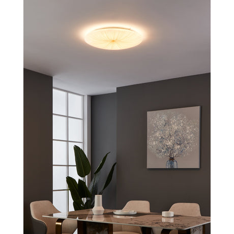 Nieves 1 LED flush ceiling light, 51cm round white fixture with radiating gold-line pattern, illuminated above a dining area with dark walls and decor.