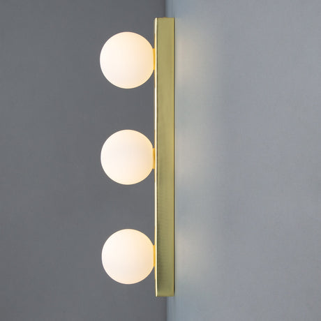 Noelani Triple Glass Globe Wall Light IP44 in brass with three frosted glass globes stacked on a slim vertical bar, mounted against a grey background.