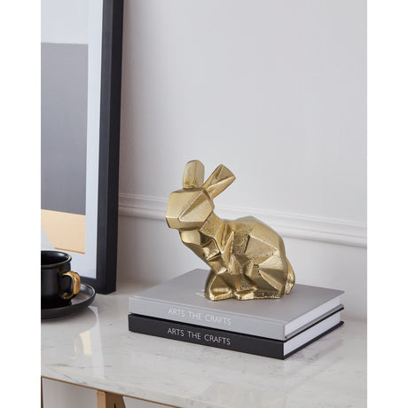 Nolalu Rabbit Ornament in gold-finish aluminium with faceted geometric design, displayed on stacked books on a marble console table.