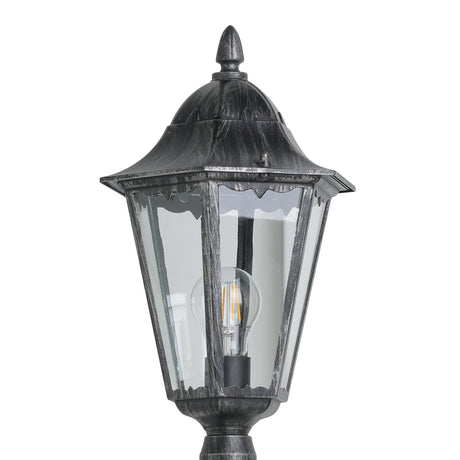Close-up of a Nolmane lamp post with hexagonal lantern head, clear glass panels, black cast aluminium finish with silver patina, pointed finial, and E27 bulb, on a white background.