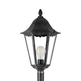 Nolmane outdoor floor lamp with a hexagonal glass-paned lantern head, curved canopy, pointed finial and visible E27 bulb, in black aluminium with silver patina, shown on a plain white background.
