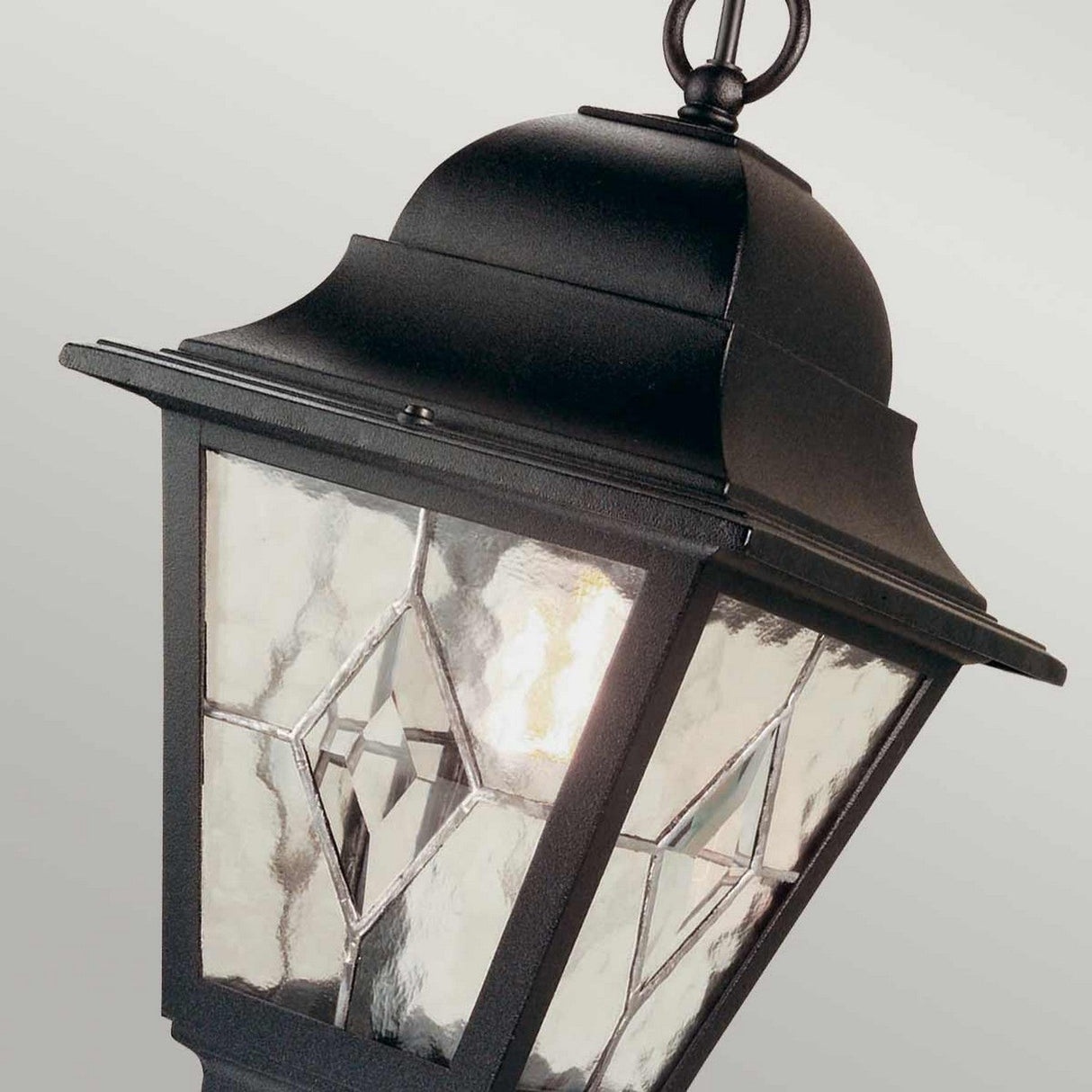 A close-up of the Norfolk 1 Light Outdoor Chain Pendant - Black highlights its lantern-inspired design, featuring decorative hand-leaded glass panes with geometric patterns. Slightly tilted, it elegantly showcases its classic style against a neutral background.