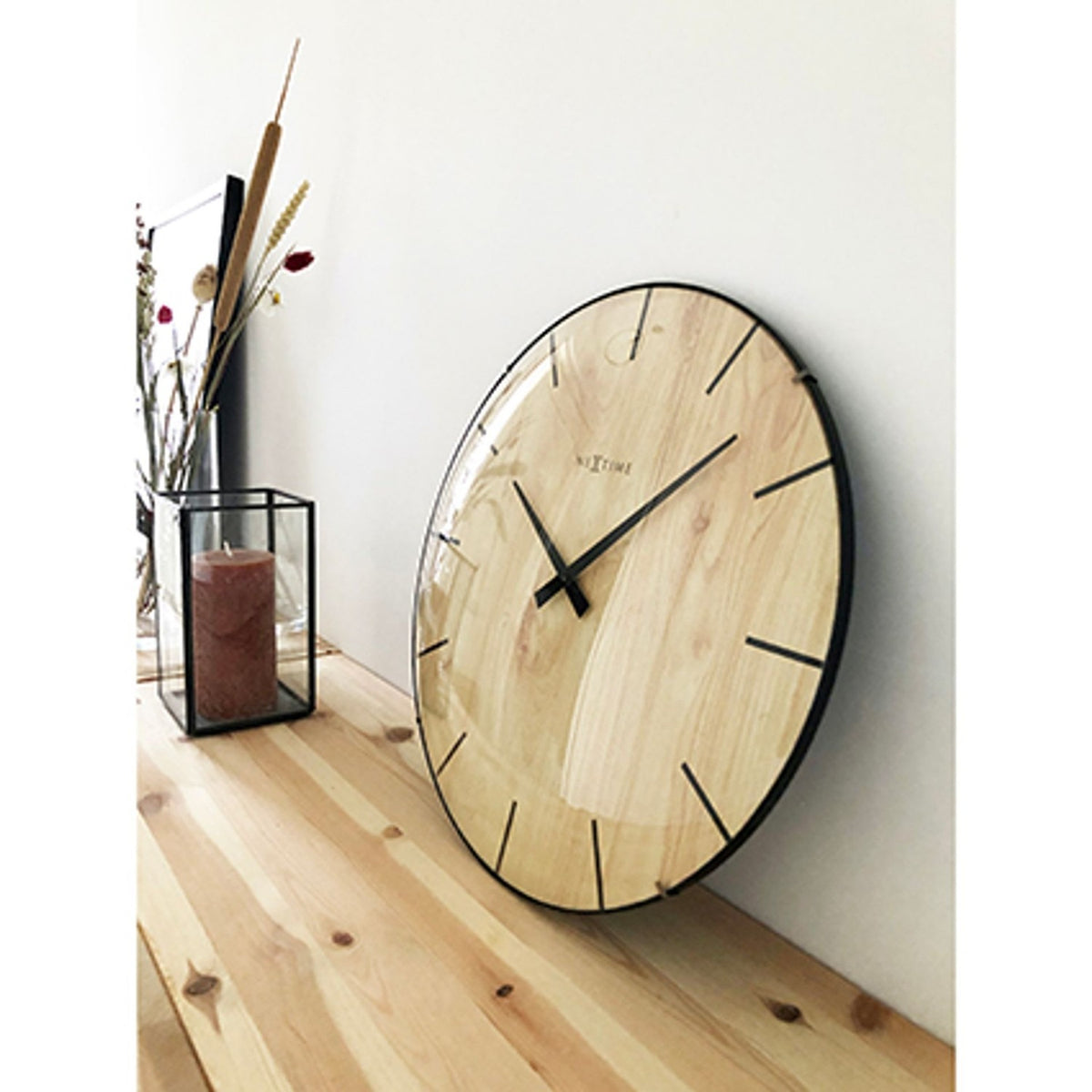 Round 35cm wall clock with brown wood-grain dial and domed glass front, black baton markers and hands, black rim, shown leaning against a wall on a wooden floor.