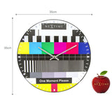 Round 35cm wall clock with domed glass face featuring a TV test card design in bold color bars, black and white stripes, and silver hands, shown on a white background.