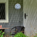 Poppy Galvanised Deep Round Wall Clock 22cm in silver with white dial, mounted on exterior wall siding beside a door in a rainy outdoor porch setting.