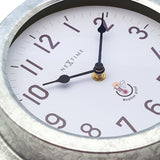 Close-up of the Poppy round wall clock showing the white dial with bold numerals, slim black hands, and deep galvanised silver case.