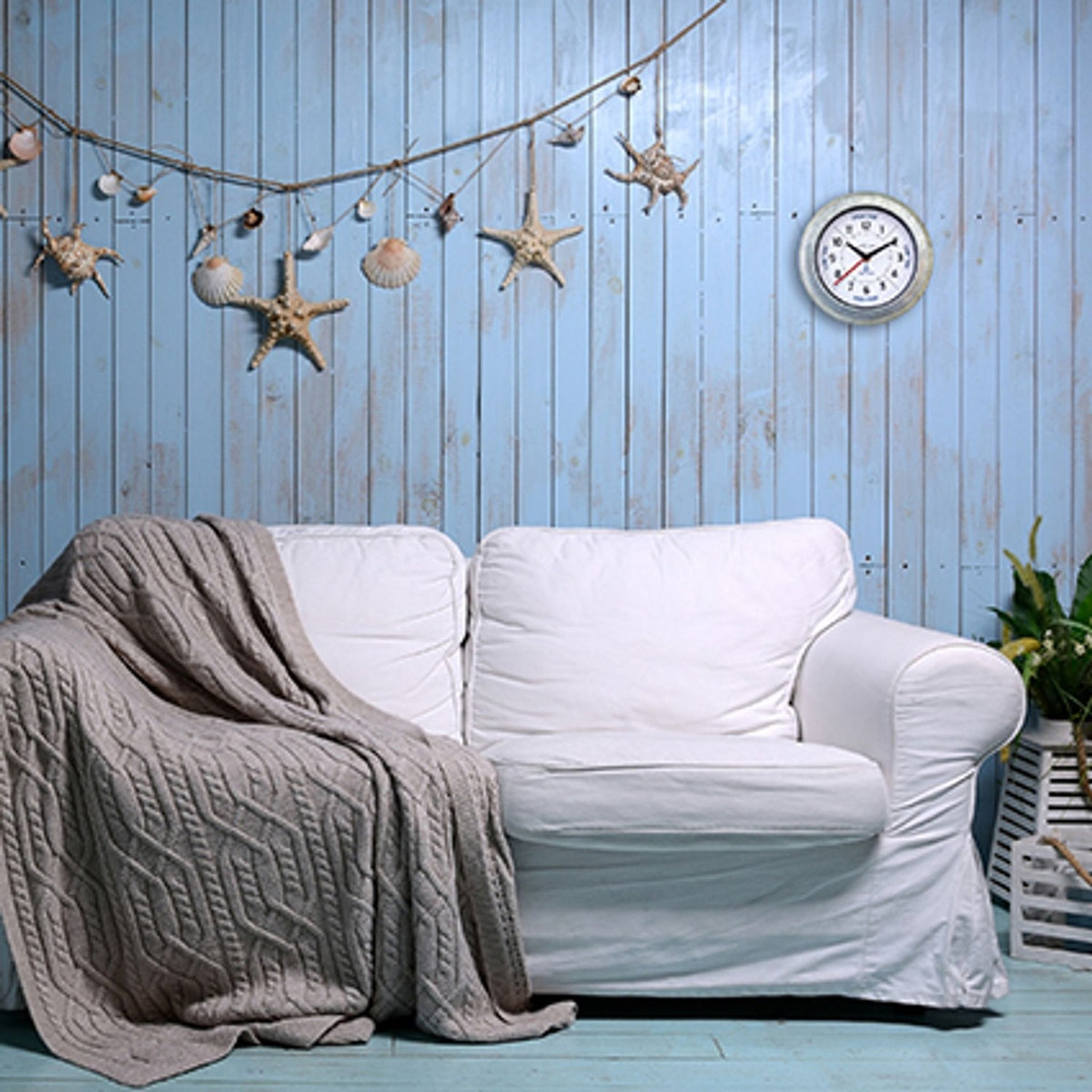 Tide Galvanised Wall Clock with Anchor Dial 22cm in silver, round case with white dial and black hands, mounted on a blue panelled wall above a white sofa.