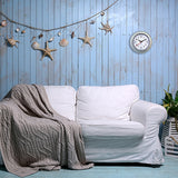 Tide Galvanised Wall Clock with Anchor Dial 22cm in silver, round case with white dial and black hands, mounted on a blue panelled wall above a white sofa.