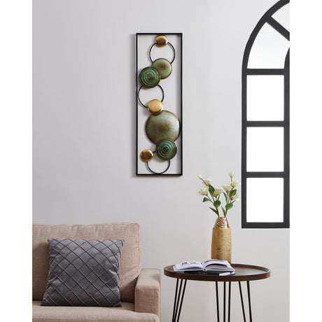 Numazu Wall Decoration 30 x 3cm in a slim black rectangular frame with linked rings holding sage-green spiral discs and textured gold circles, mounted on a light wall above a living room sofa.