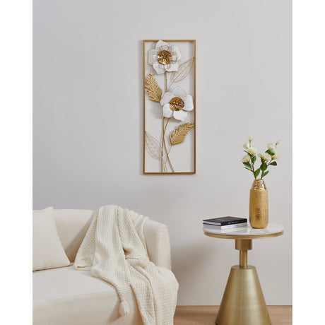 Numazu Wall Decoration in gold and white, a slim rectangular metal panel with two flowers, gold fronds and leaf outlines, displayed above a cream sofa in a living room.