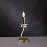 The Nydia 1 Light Crystal Table Lamp in French gold features a star-shaped crystal accent and a round base, displayed on a gray surface against a dark background.