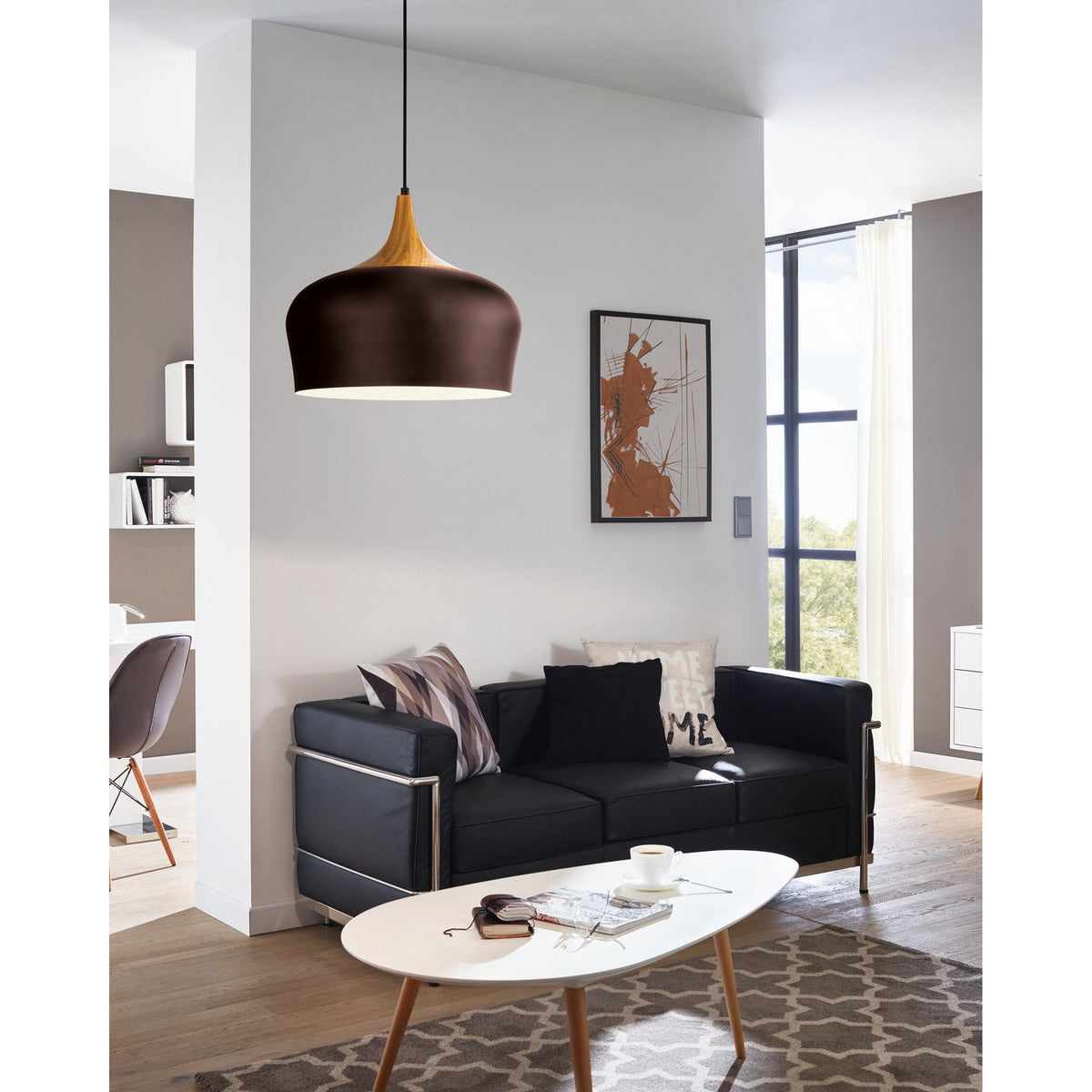 Obregon Pendant Light in brown steel with cream interior and oak-toned crown, dome shade on black cable, shown above a black sofa in a living room setting.