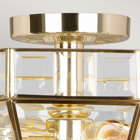 Close-up of the Old Park 2 Light Semi Flush in polished brass. The geometric design, crafted from polished brass and transparent glass panels, exudes luxury and elegance. The image focuses on the top section of this chandelier against a light background.