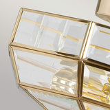 A close-up view of the Old Park 2 Light Semi Flush with polished brass accents and clear glass panels. The design reflects light, producing a prismatic effect on a gentle, neutral gradient backdrop.