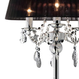 A close-up of the Olivia 3 Light Crystal Floor Lamp in chrome, featuring a black pleated shade and hanging crystal accents on a shiny base, softly illuminated with warm light.