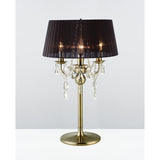 The Olivia 3 Light Crystal Table Lamp features an antique brass base, black pleated shade, and crystal accents hanging from its arms, all set against a plain white background.