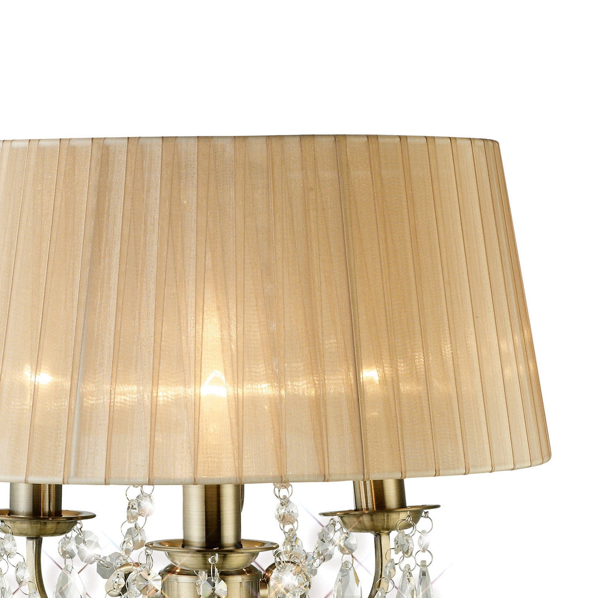 A close-up of the Olivia 3 Light Crystal Table Lamp in antique brass features a bronze pleated shade and hanging crystal accents. The lamp is lit, casting a warm, inviting glow.