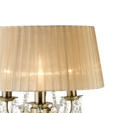 A close-up of the Olivia 3 Light Crystal Table Lamp in antique brass features a bronze pleated shade and hanging crystal accents. The lamp is lit, casting a warm, inviting glow.