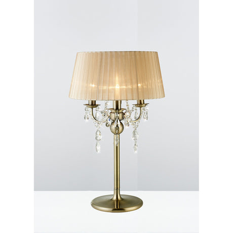 The Olivia 3 Light Crystal Table Lamp in antique brass with a bronze shade and crystal accents sits on a white surface against a light background.