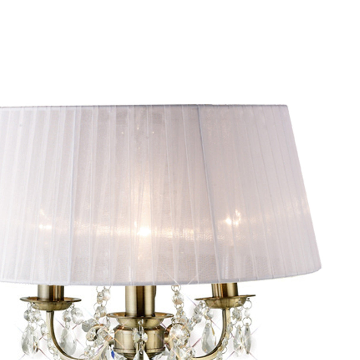 The Olivia 3 Light Crystal Table Lamp features an antique brass base, ornate arms, hanging crystal accents, and a sheer white fabric drum shade. When lit, it creates a soft glow—ideal for elegant interior lighting.