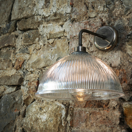 Olvane Ribbed Glass Wall Light IP65 with a clear dome shade on an antique silver L-shaped arm and round wall plate, mounted on a stone wall.