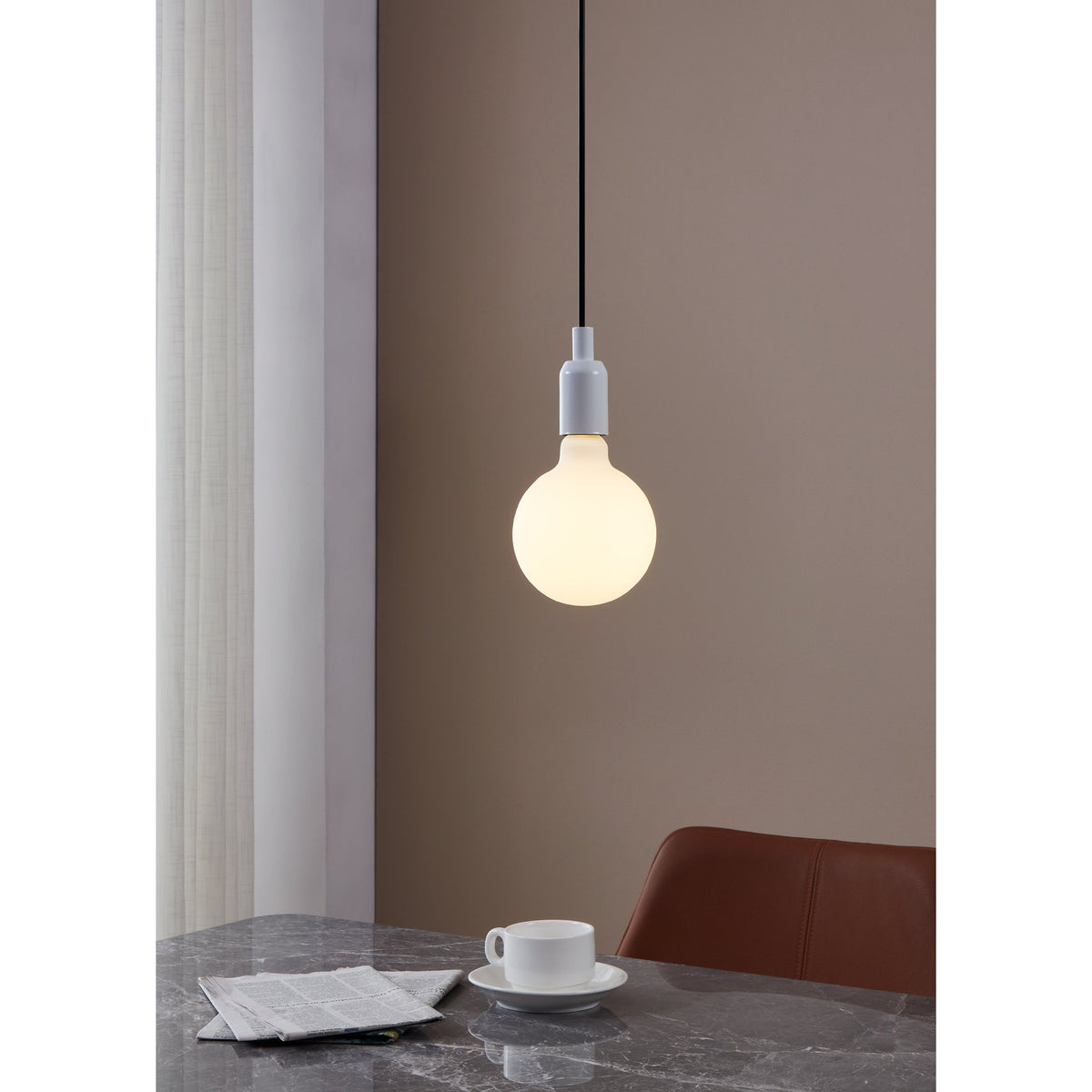Opal Dimmable LED Globe Bulb E27 G125 glowing warm white in a white pendant fitting above a marble dining table set with a teacup and newspaper.