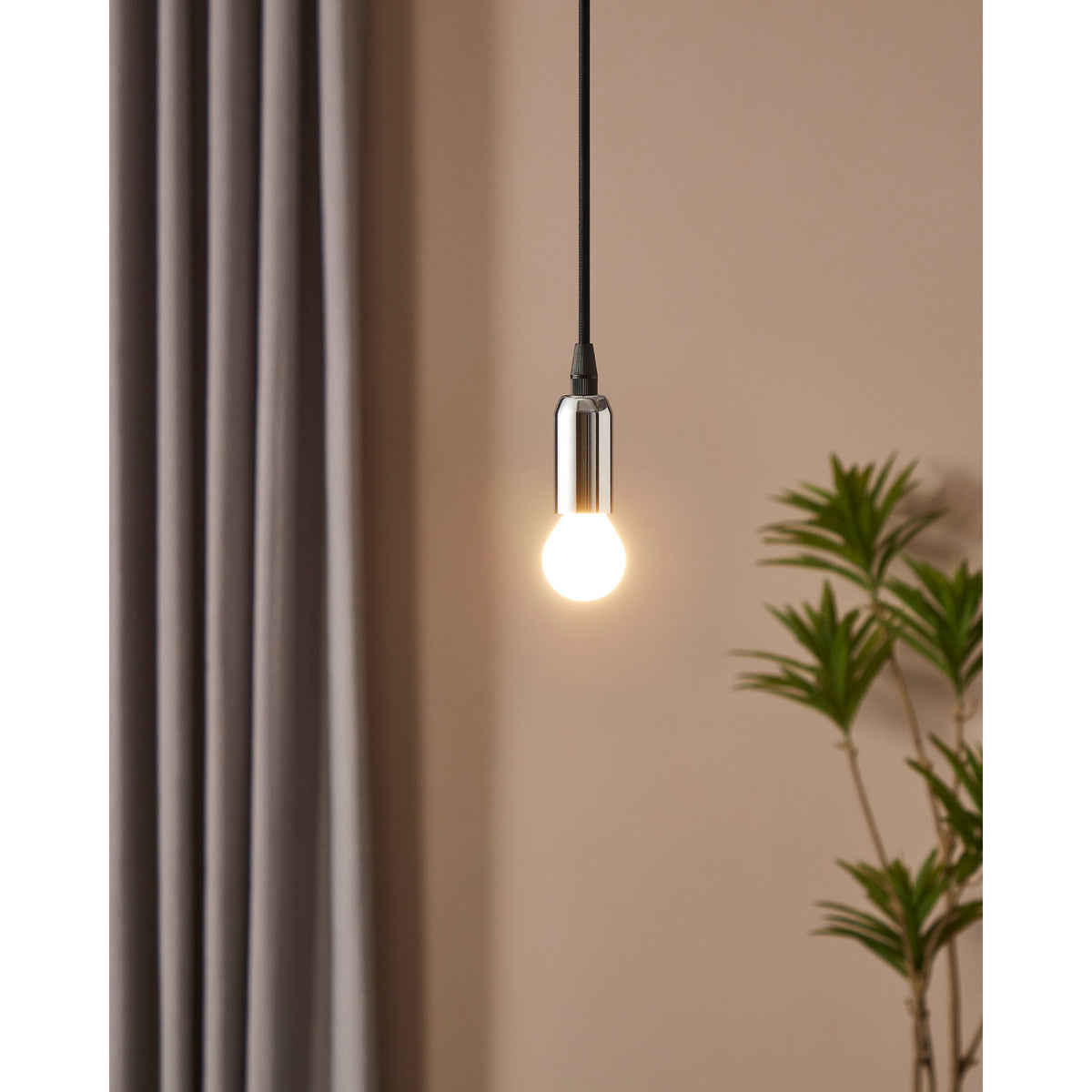 Pendant light with chrome holder and black cable fitted with an Opal Dimmable LED Golf Ball Bulb E14, glowing warm white against a beige wall with curtains and a potted plant.