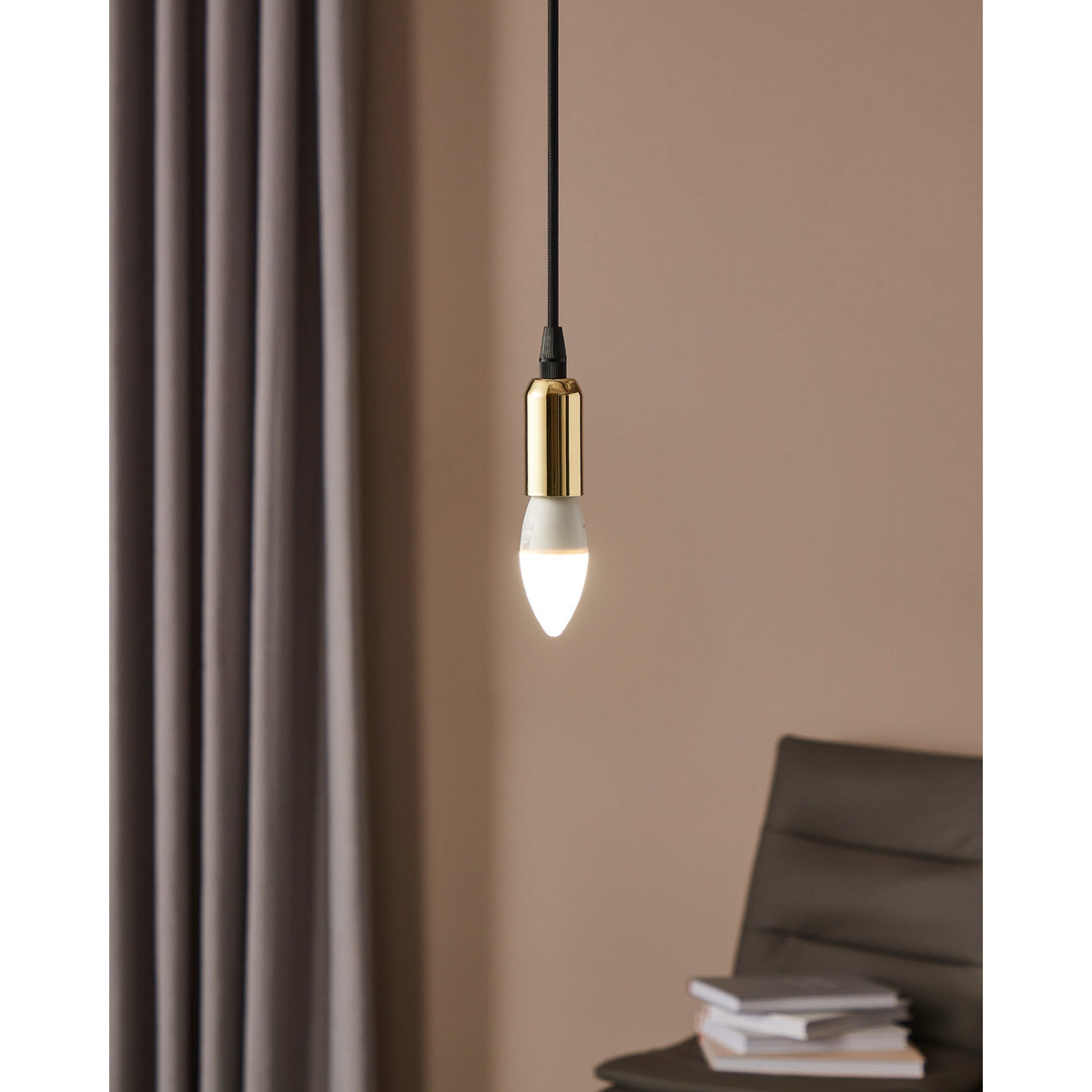Opal LED Bulb E14, lit in a brass pendant fitting, shown hanging in a room with taupe curtains, a dark armchair, and stacked books.