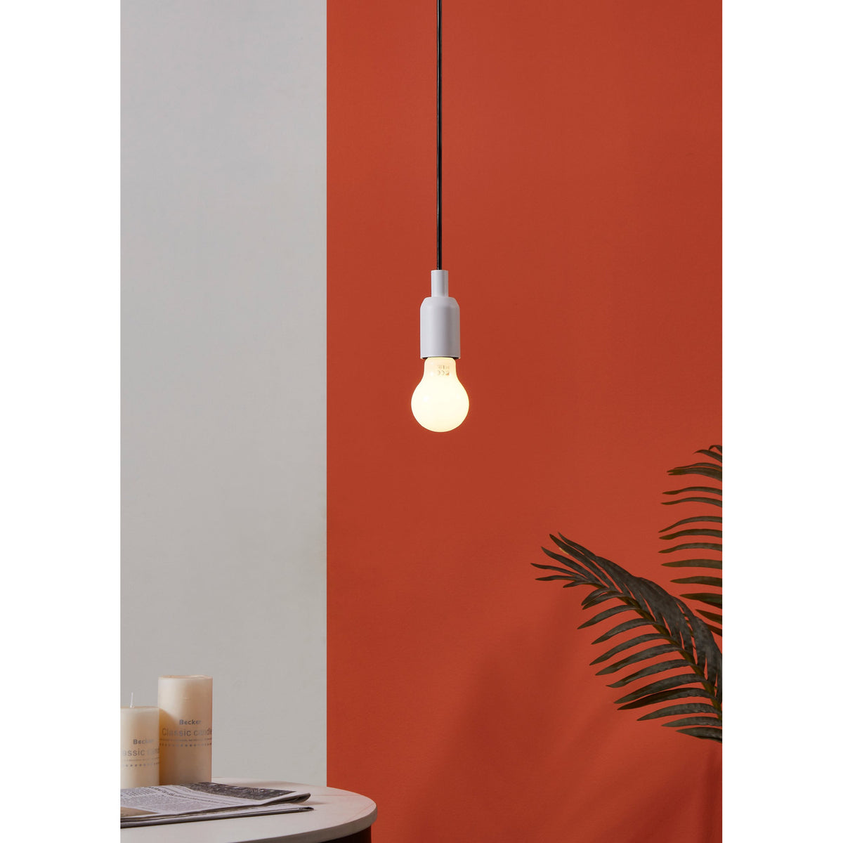 Opal LED GLS Bulb E27 A60 4W warm white, lit in a white pendant fitting against a terracotta wall in a room setting with a side table and plant.
