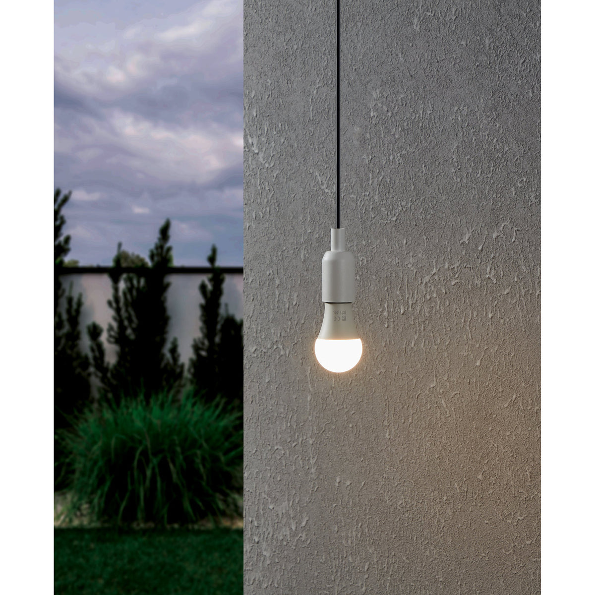 Opal LED GLS bulb with E27 screw cap, pear-shaped white plastic shade, shown lit and suspended outdoors against a textured grey wall at dusk.