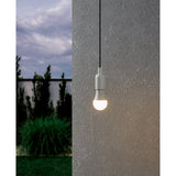 Opal LED GLS bulb with E27 screw cap, pear-shaped white plastic shade, shown lit and suspended outdoors against a textured grey wall at dusk.