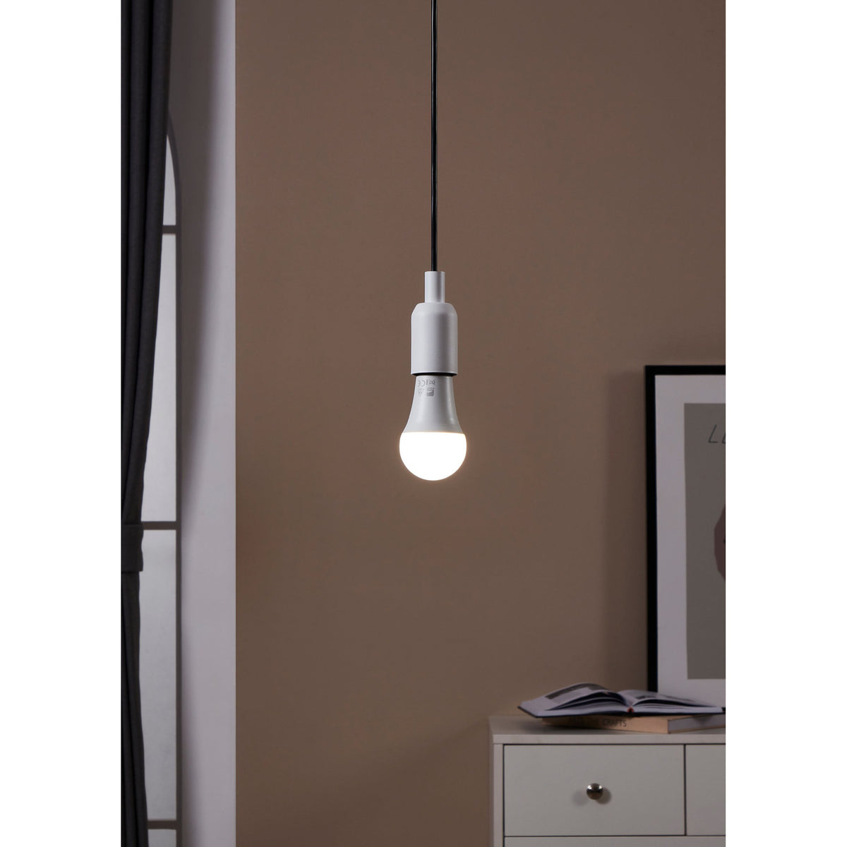Opal LED GLS bulb, E27 screw cap, A60 shape, lit warm-white in a white pendant fitting against a brown wall in a living room setting.