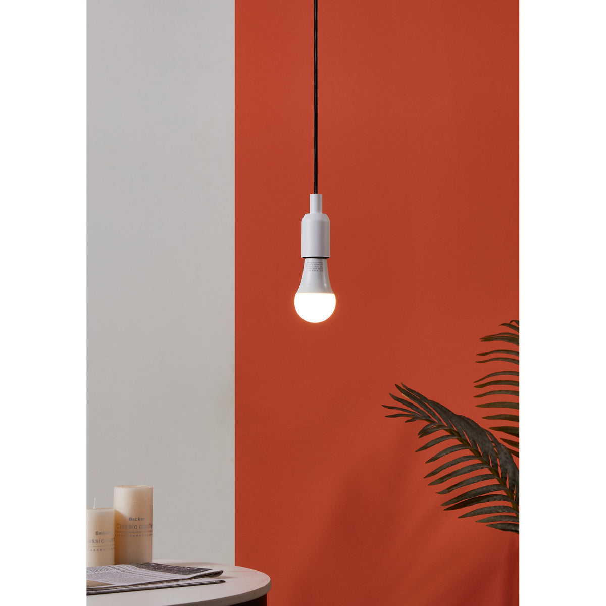 Opal LED GLS bulb, E27 fitting, lit warm white in a pendant fixture with black cable, against a terracotta wall in a styled room setting.
