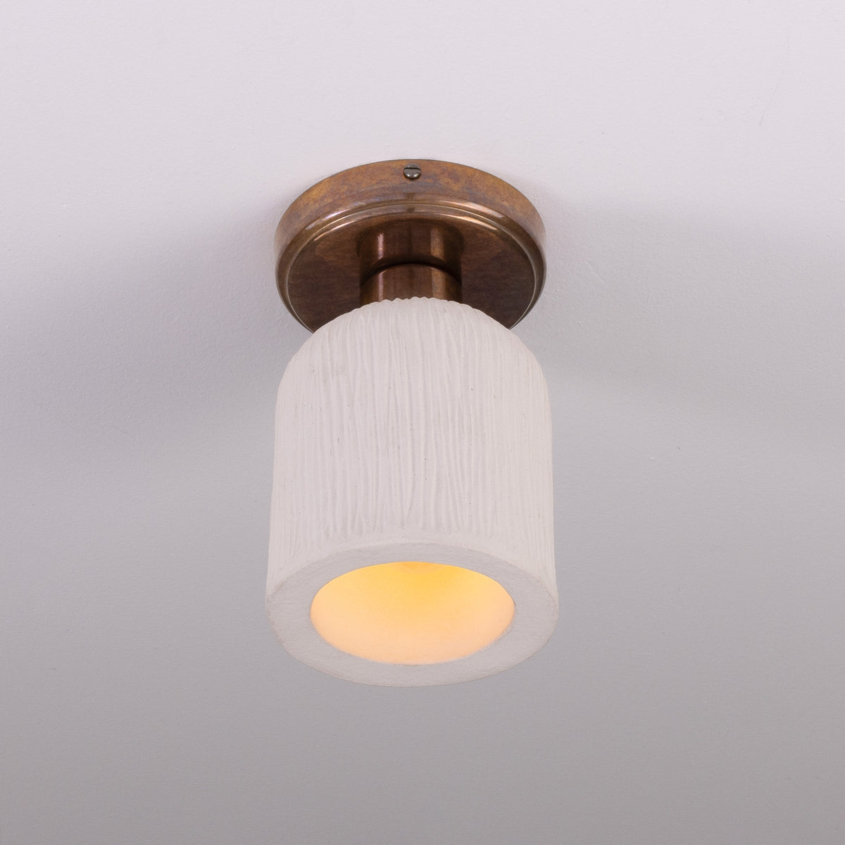 Osier Ceramic Flush Ceiling Light with matt white striped ceramic shade and round brass ceiling plate, lit from below, on a plain white background.