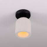 Osier Ceramic Flush Ceiling Light with a matt white striped cylindrical ceramic shade on a round black ceiling plate, warm bulb glow visible, plain light grey background.